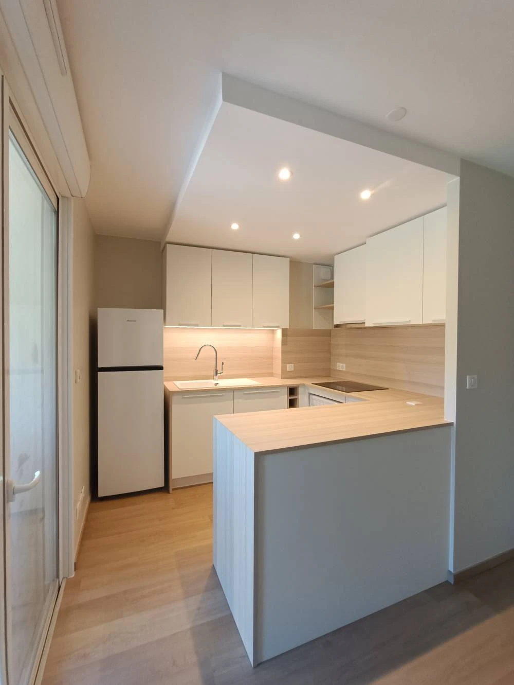 Cuisine minimaliste blanche avec une colonne d'appareils encastrés intégrant deux fours Whirlpool inox côte à côte, tiroirs et placards à poignées noires linéaires