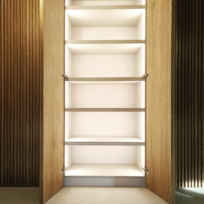 Chambre d'hôtel style chalet alpin, mur en vieux bois massif vertical, lit double blanc immaculé, armoire intégrée en bois brut avec portes coulissantes en planches obliques, intérieur laqué beige avec étagères blanches et linge plié