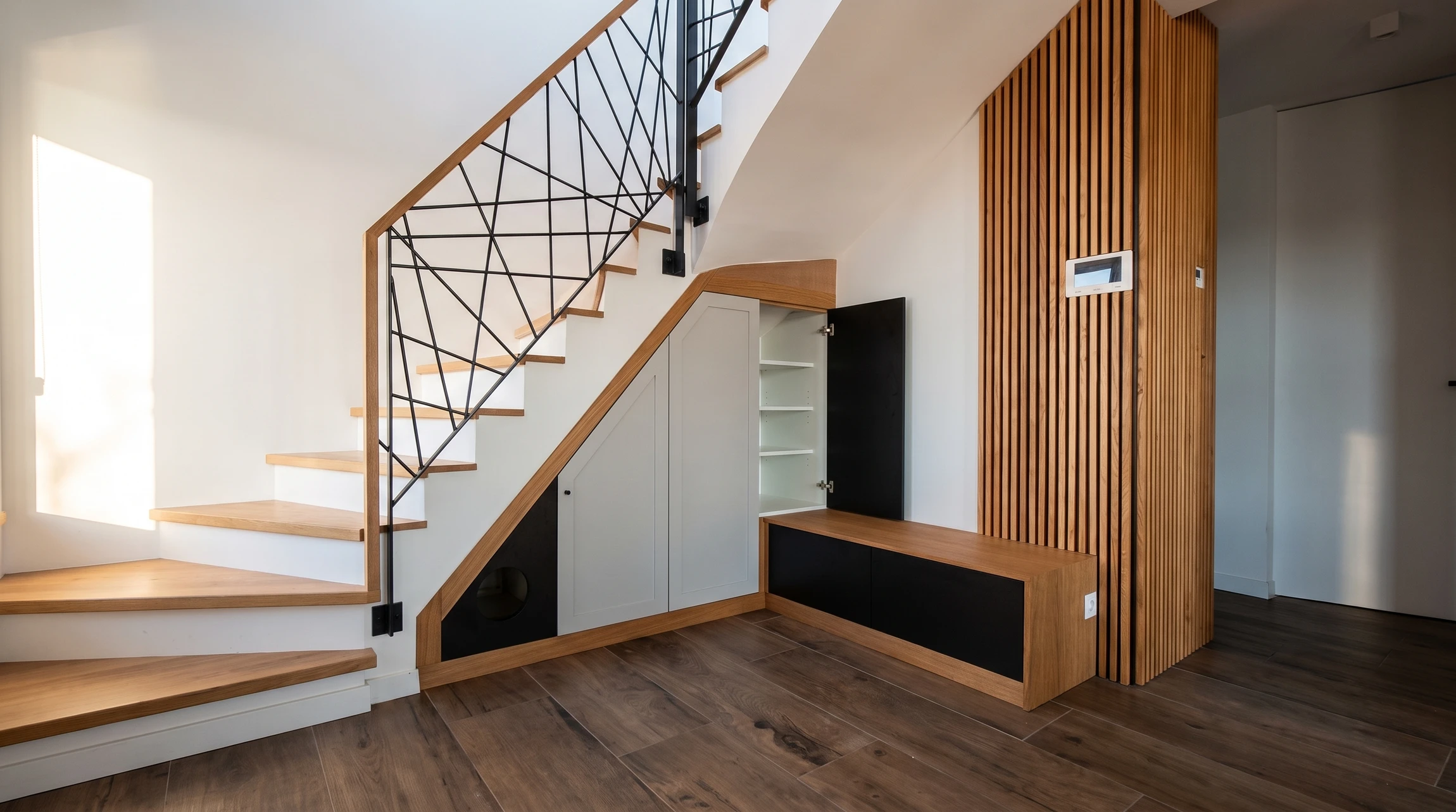 Photographie professionnelle d'un intérieur moderne montrant un espace étroit ou sous-utilisé (recoin, niche murale, espace sous escalier ou coin mort) avant optimisation, avec zones ombrées et peu exploitées. Puis en parallèle ou superposition progressive, la même zone intégralement aménagée sur mesure avec mobilier intégré (rangements encastrés, étagères, tiroirs coulissants, niches) utilisant chaque centimètre vertical et horizontal. Matériaux nobles : bois massif (chêne, noyer), quincaillerie premium (Blum), finitions laquées ou naturelles. Éclairage LED discret intégré. L'image doit démontrer concrètement comment un espace chaotique ou vide devient fonctionnel et esthétique grâce au sur-mesure.